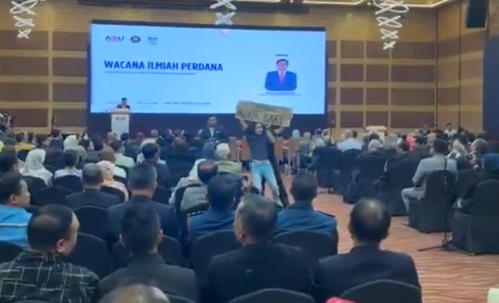 社运分子在阿占巴基演说途中，高举“逮捕阿占巴基”的大字报，引起在场者注意。-图截自视频-