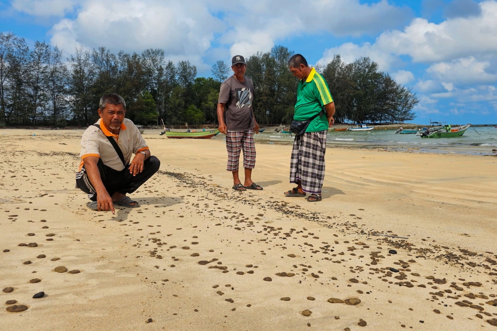 52岁渔夫纳兹里赛益与同伴周三指出直落卡隆海滩上的斑点，相信是自周一以来停泊在附近海域的一艘船只的油污。-马新社-