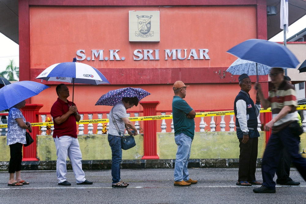 麻坡周六早上下雨，投票中心的选民撑伞排队等待投票。-马新社-