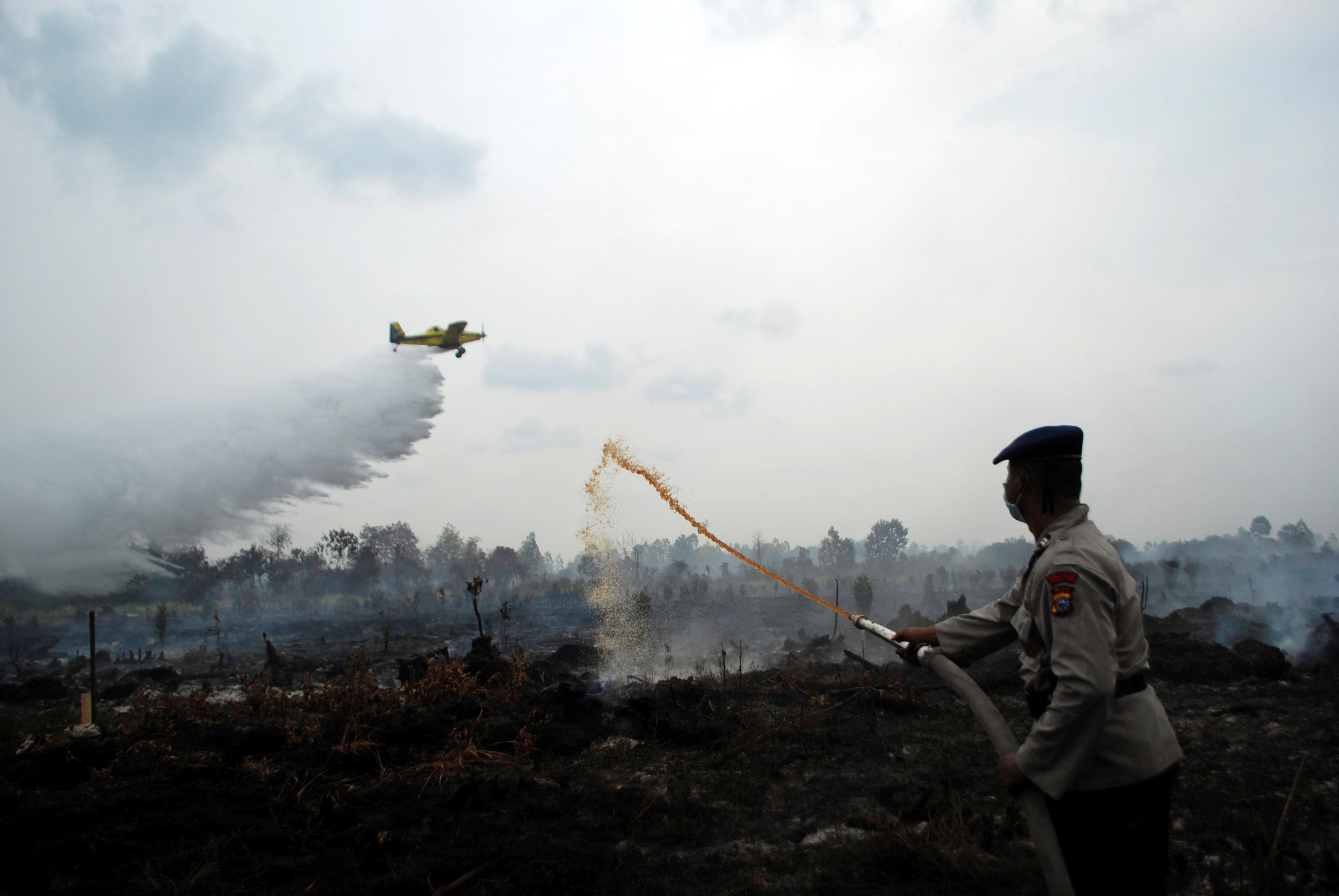 A water bomber drops its payload as a police officer tries to extinguish a peat fire in Kampar, Riau province, Sumatra, Indonesia August 29, 2016 in this photo taken by Antara Foto. Antara Foto/Rony Muharrman/via REUTERS ATTENTION EDITORS - THIS IMAGE WAS