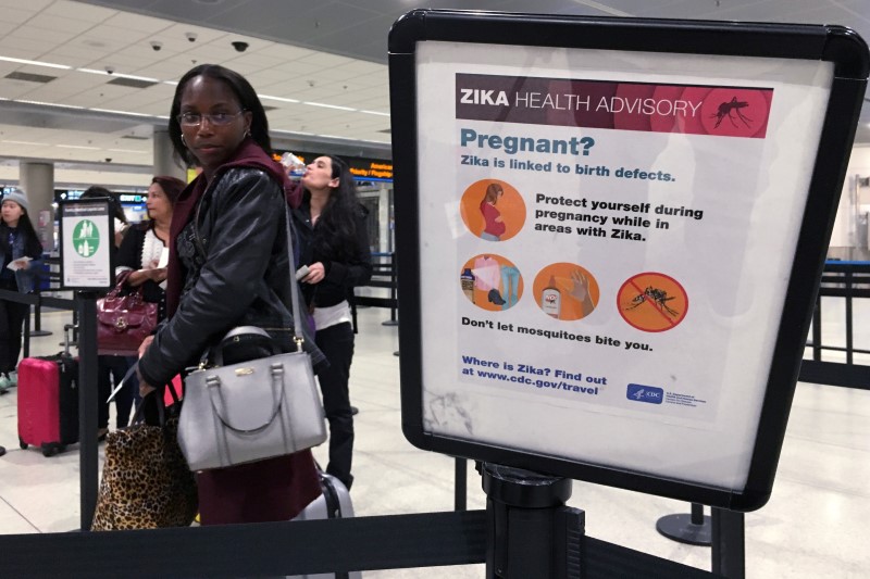 A woman looks at a Center for Disease Control (CDC) health advisory sign about the dangers of the Zika virus as she lines up for a security screening at Miami International Airport in Miami, Florida, U.S., May 23, 2016. REUTERS/Carlo Allegrin