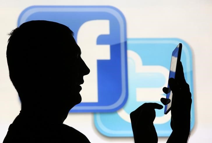 A man is silhouetted as he uses a mini tablet computer while standing in front of a video screen with the Facebook and Twitter logos, in this picture illustration taken in Sarajevo October22, 2013.u00c2u00a0u00e2u20acu201d Reuters pic
