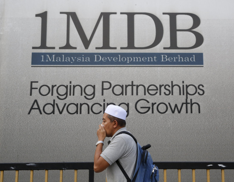 A man covers his mouth as he walks past a 1Malaysia Development Berhad (1MDB) billboard at the funds flagship Tun Razak Exchange development in Kuala Lumpur, February 27, 2015. u00e2u20acu201d Reuters pic
