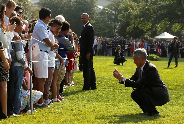 李显龙（蹲者）在奥巴马引领与观礼民众握手致意时，自己还当起摄影师帮民众拍照。-路透社-