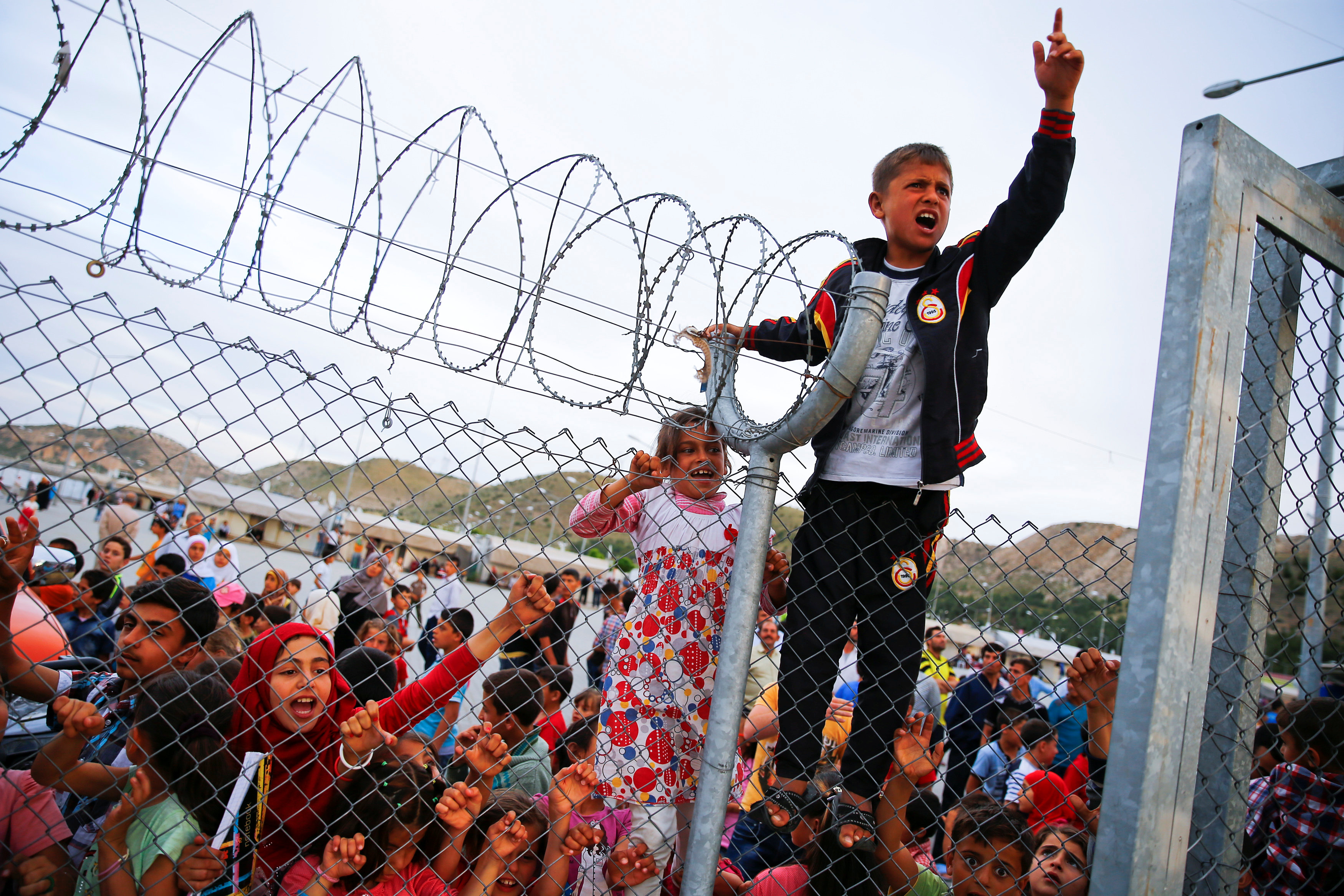 Refugee youths gesture from behind a fence as German Chancellor Angela Merkel, Turkish Prime Minister Ahmet Davutoglu, EU Council President Donald Tusk and European Commission Vice-President Frans Timmermans (all not pictured) arrive at Nizip refugee camp