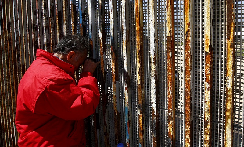 在墨西哥边境城市蒂华纳（Tijuana），一名男子隔着围墙向身在美国境内的亲人说话。-路透社-