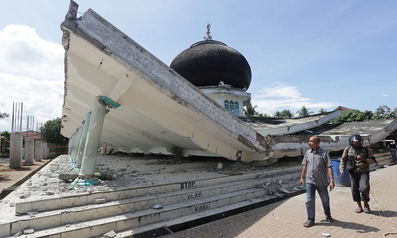 People walk near a collapsed mosque following an earthquake in Meuredu, Pidie Jaya in the northern province of Aceh, Indonesia December 7, 2016 in this photo taken by Antara Foto. Antara Foto/ Irwansyah Putra/via REUTERS ATTENTION EDITORS - THIS IMAGE WAS