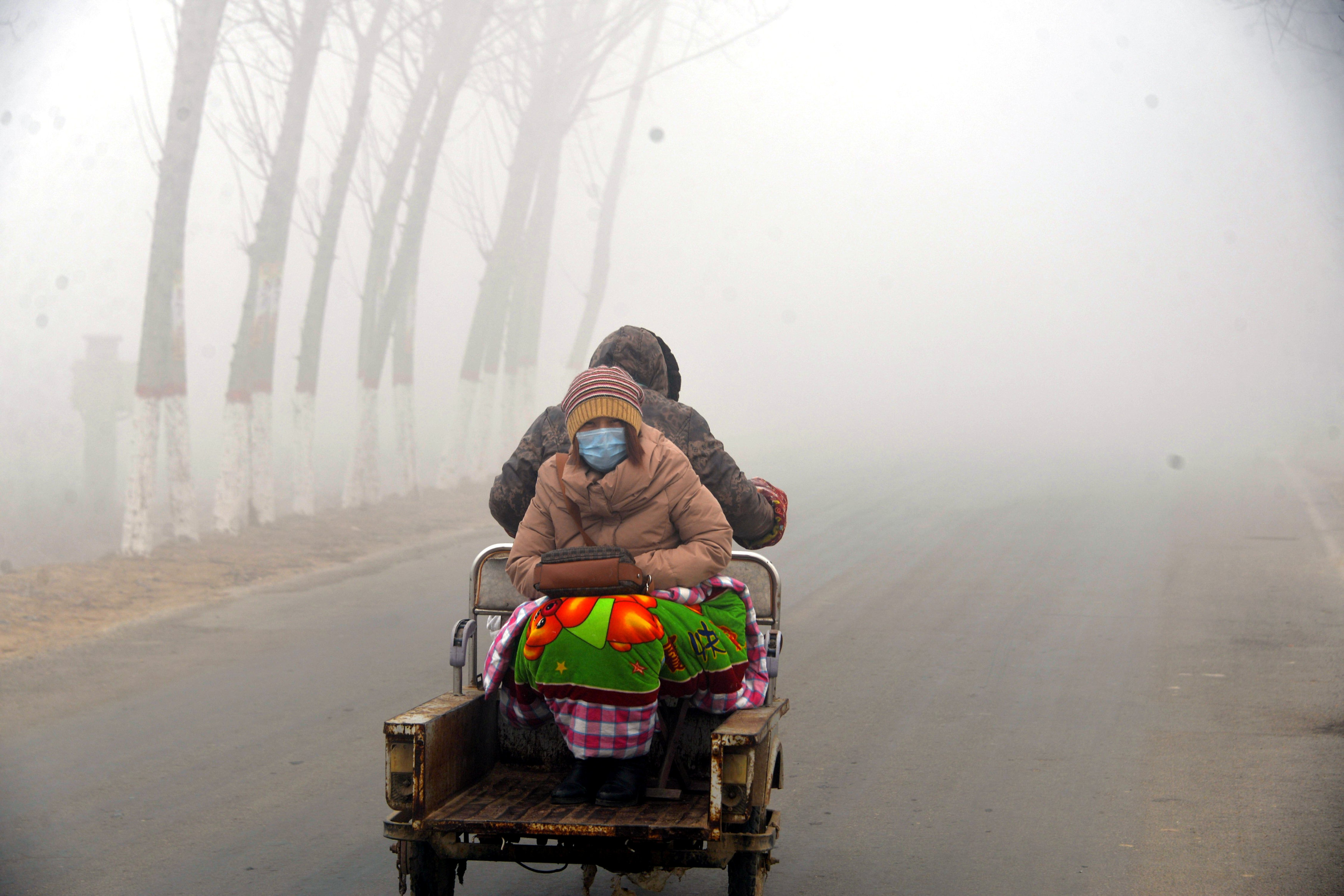 A woman sits on the back of a motorcycle in smog during a polluted day in Liaocheng, Shandong province, China, December 19, 2016. REUTERS/Stringer ATTENTION EDITORS - THIS PICTURE WAS PROVIDED BY A THIRD PARTY. EDITORIAL USE ONLY. CHINA OUT. NO COMMERCIAL