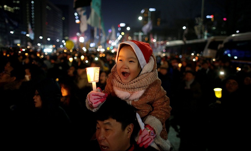 A child sitting on his father's shoulder holds a candlelight during a protest demanding South Korean President Park Geun-hye's resignation in Seoul, South Korea, December 24, 2016. REUTERS/Kim Hong-Ji