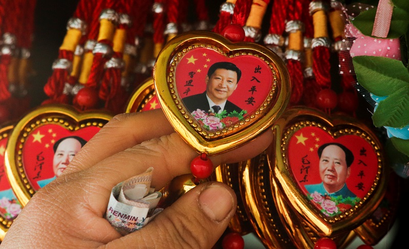 A woman picks a souvenir necklace with a portrait of Chinese President Xi Jinping from a selection that also includes necklaces featuring late Chinese Chairman Mao Zedong at a stall in Tiananmen Square in Beijing, China, February 26, 2018. REUTERS/Thomas 