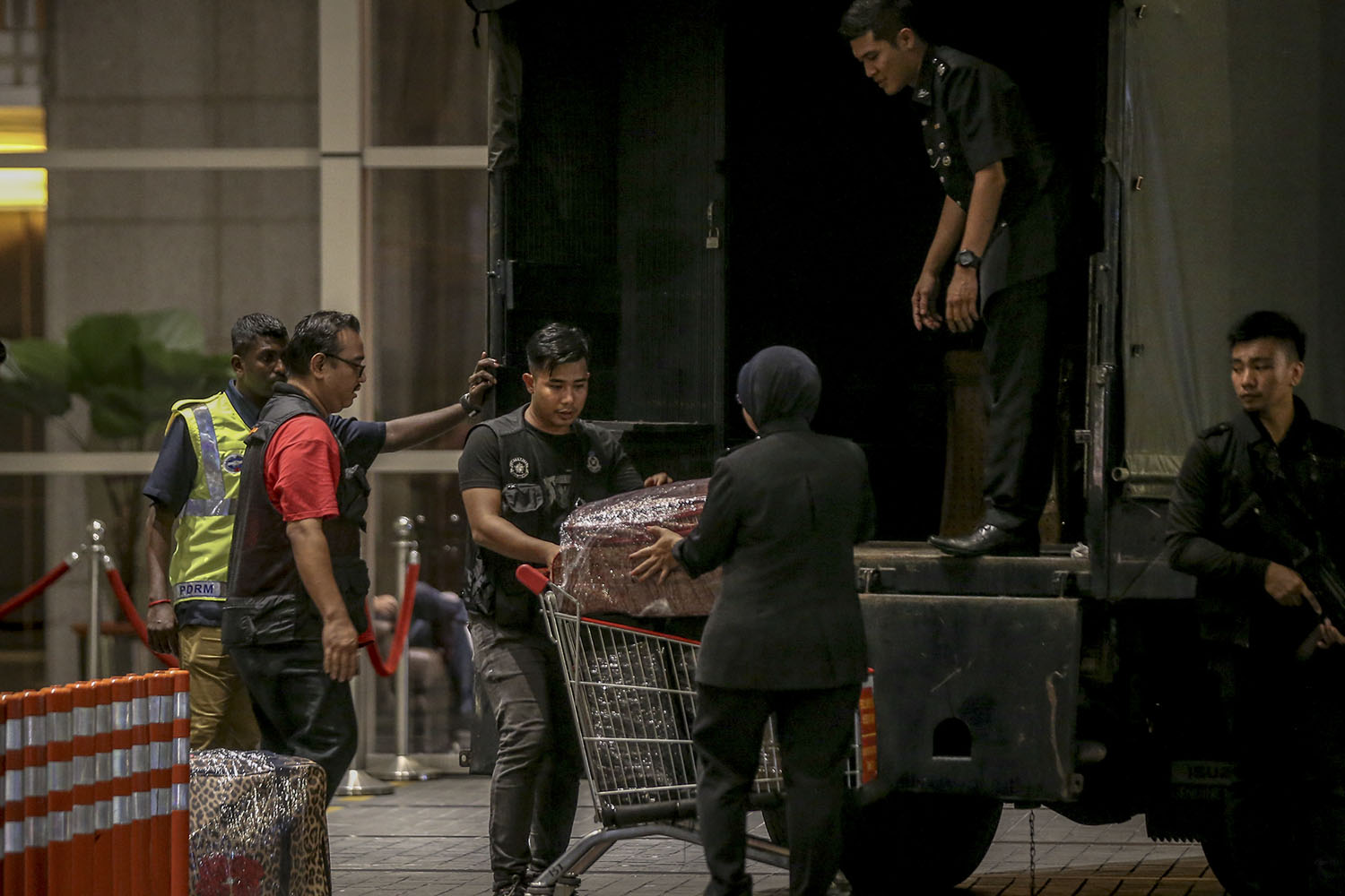 Police personnel lift suitcases filled with cash and jewellery onto a waiting Black Maria outside the Pavilion Residences. u00e2u20acu201d Picture by Hari Anggara