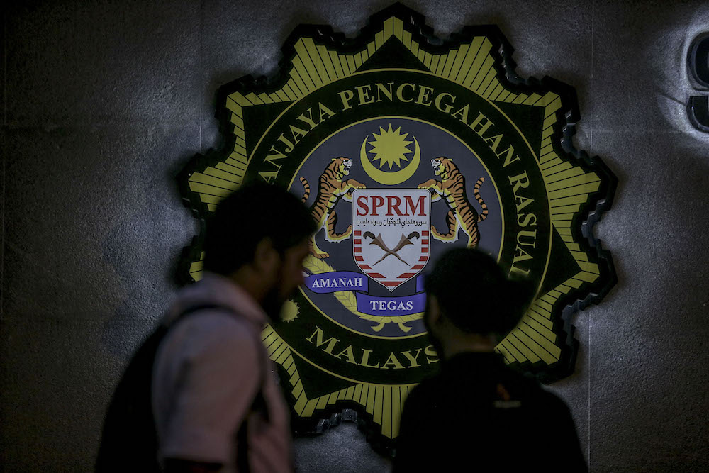 Two members of the media stand against the backdrop of the MACC  logo in Putrajaya July 3, 2018. u00e2u20acu201d Picture by Hari Anggara