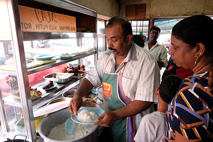 正在为顾客盛饭淋咖哩汁的老板阿杜阿哈杜。-Steven Ooi K.E.摄-