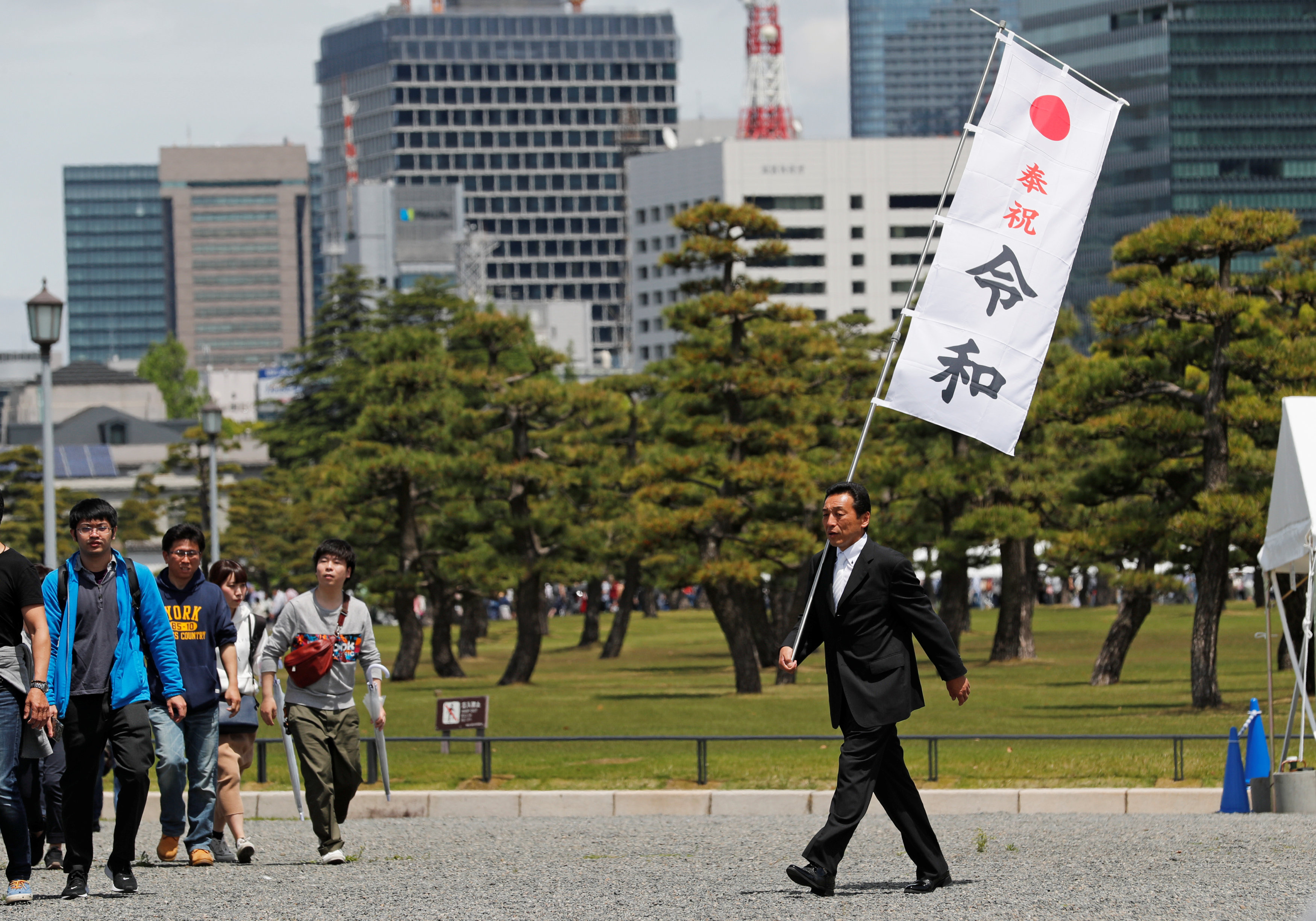 东京皇宫外，一名男子肩扛写有日本新年号“令和”的旗帜。-路透社-
