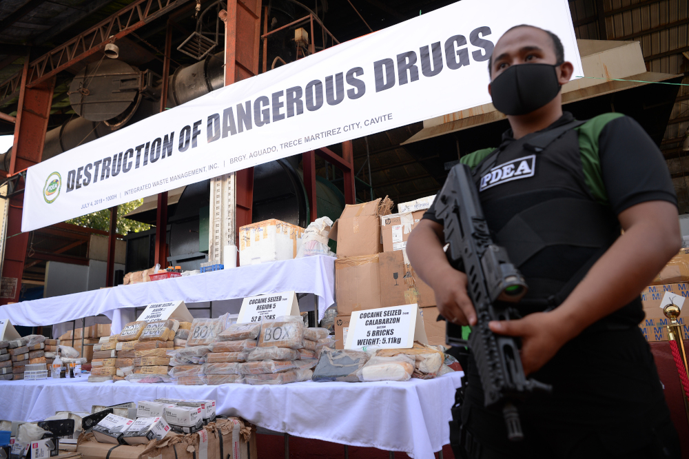 An armed agent of the Philippine Drug Enforcement Agency stands guard next to seized illegal drugs including bricks of cocaine prior to destroying them at a waste facility in Trece Martires, Cavite province July 4, 2019. u00e2u20acu201d AFP pic 