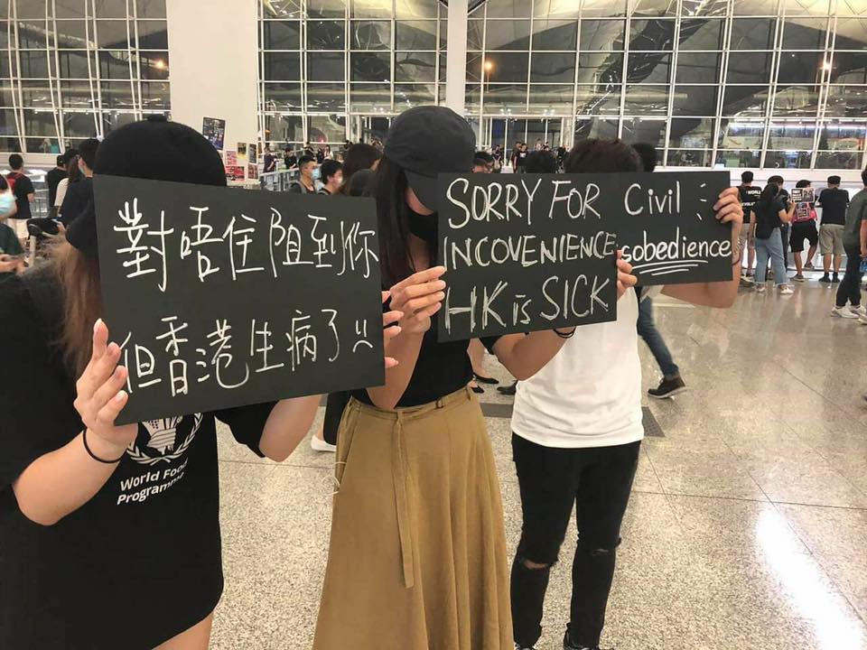 有香港青年周二在机场高举中英文标语“对唔住阻到你 但香港生病了”，向行程受到影响的旅客致歉。-图取自ChunTing Lau脸书-