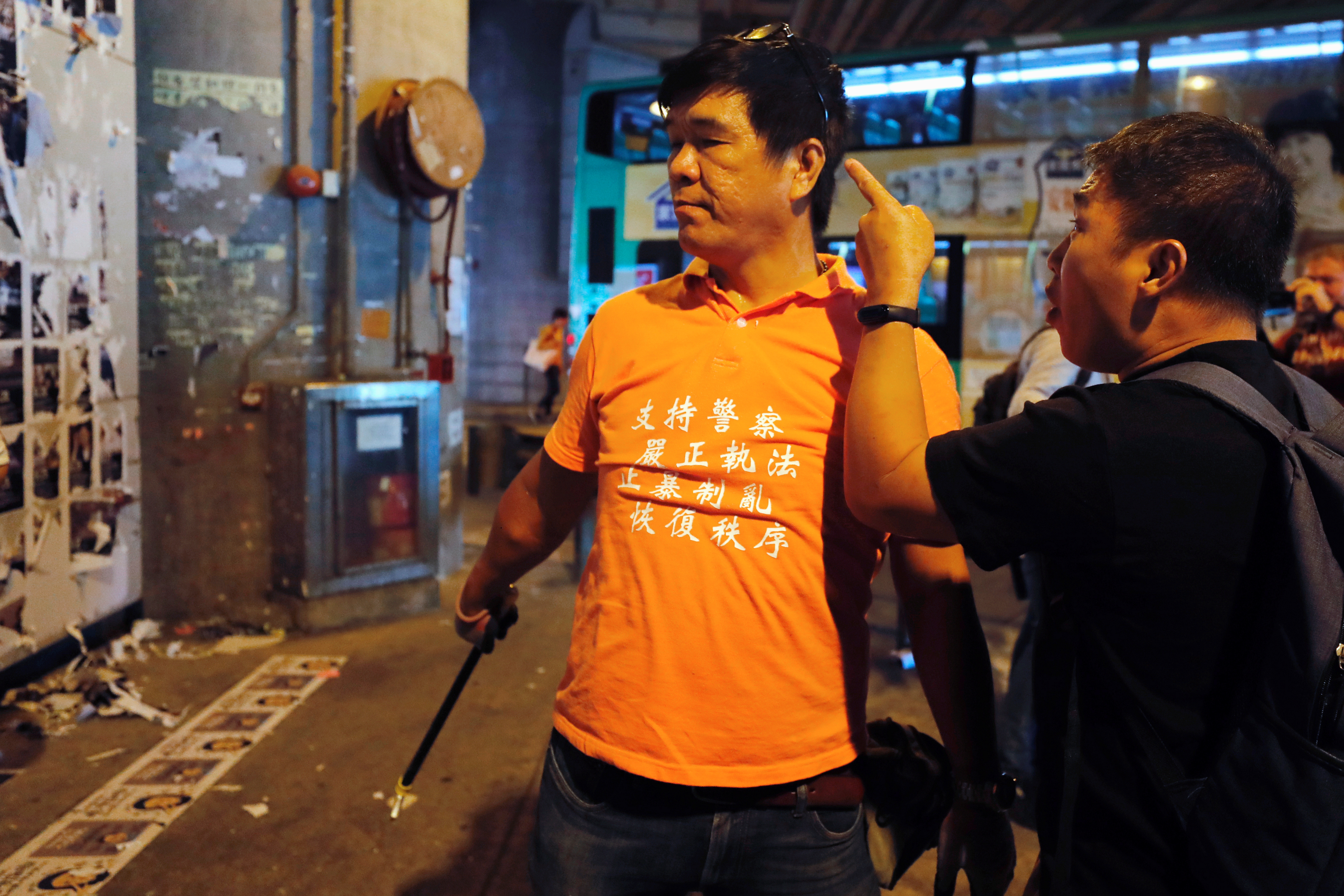 一名男子（右）指责一位穿着橙色上衣，正在清理元朗站附近的“连侬墙”的人士。-路透社-