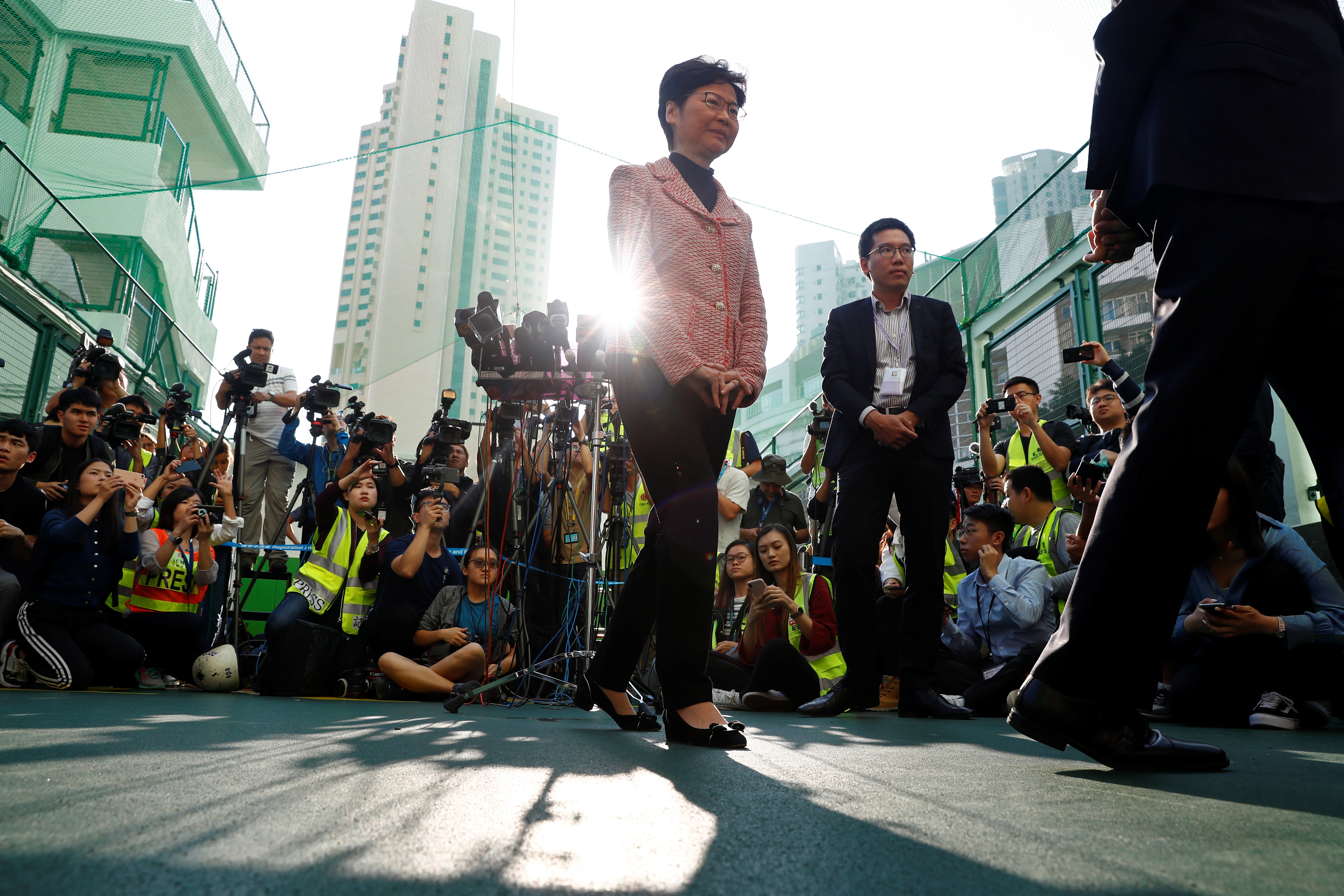 香港特首林郑月娥（红外套者）周日上午在高主教书院投票站投票，并接受媒体访问。-路透社-