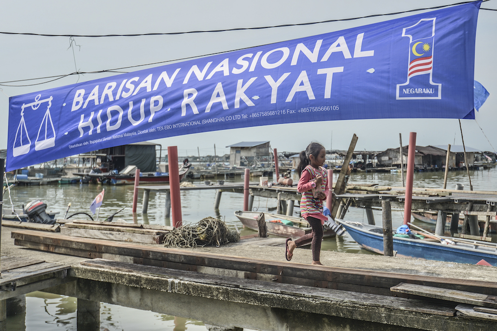 Children walk by a Barisan National banner at Kampung Air Masin in Kukup November 3, 2019. u00e2u20acu201d Picture by Shafwan Zaidon 