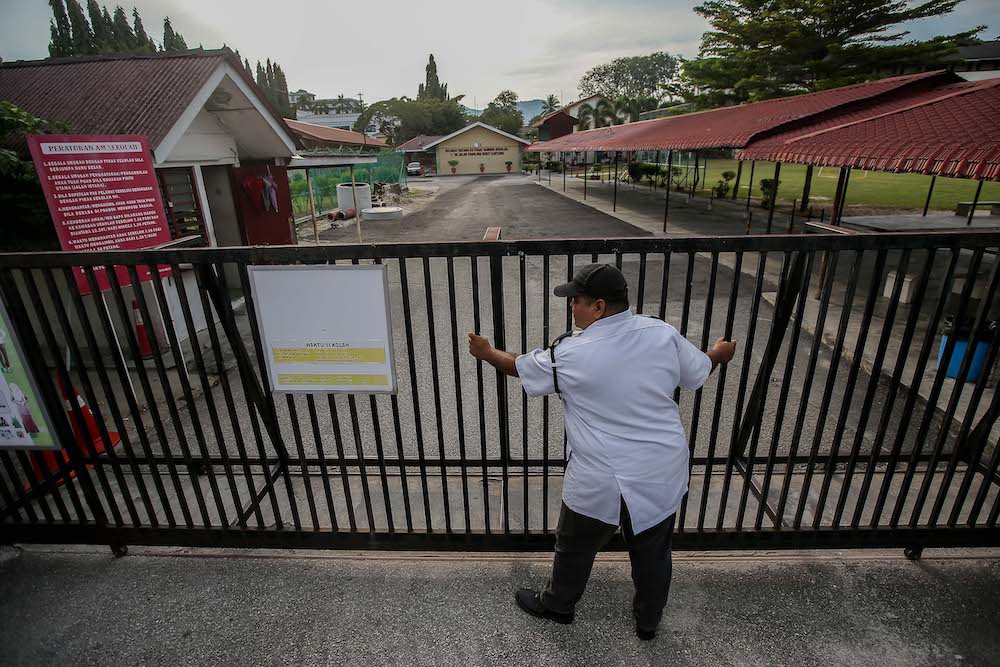 A security guard from SK Panglima Bukit Gantang Ipoh closes the school gate under a nationwide Movement Control Order from March 18 until March 31 due to the Covid-19 outbreak, March 17, 2020. u00e2u20acu201d Picture by Farhan Najib