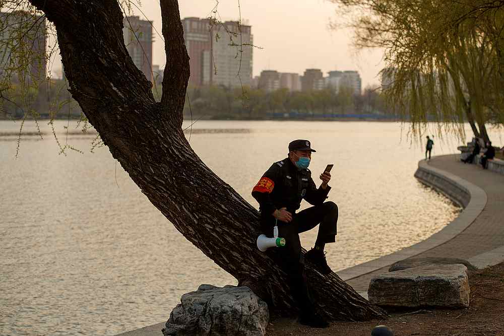 A security guard wearing a protective mask sits on a tree at a park in Beijing, China March 23, 2020.  u00e2u20acu201d Reuters pic