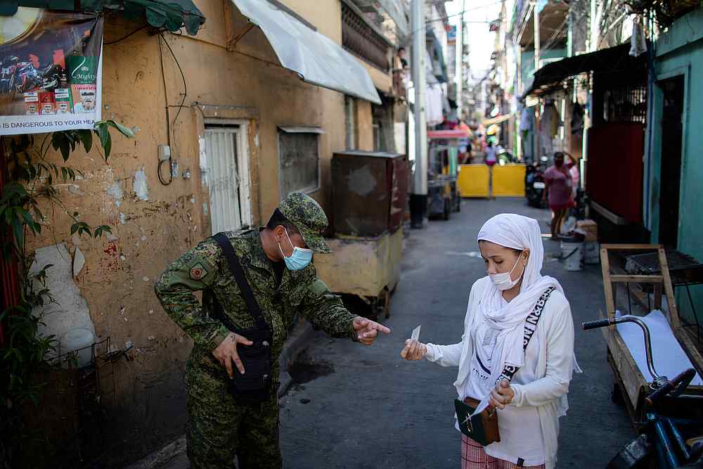 A soldier wearing a protective mask checks a woman's quarantine pass as the city undergoes a stricter lockdown to contain the Covid-19 spread, in Pasay City, Philippines April 22, 2020. u00e2u20acu201d Reuters pic