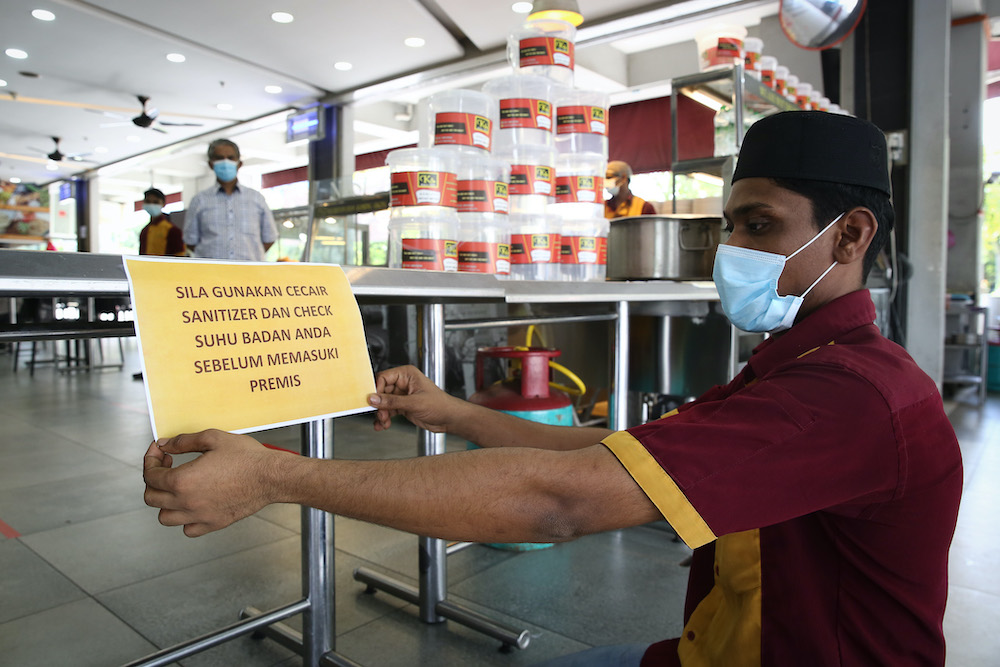 A worker places a notice of standard operating procedures at Khulafa Restaurant as eateries resume dine-in services starting May 4 in Shah Alam May 2, 2020. u00e2u20acu201d Picture by Yusof Mat Isa