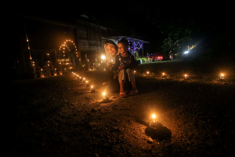 村民带着孩子开心的点燃土油灯和赏灯。-Farhan Najib摄-