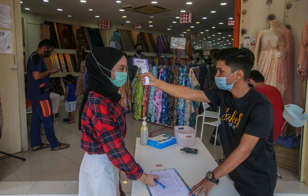 A worker takes the temperature of customers at the entrance of the Jakel Ipoh textile shop May 13, 2020. u00e2u20acu201d Picture by Farhan Najib