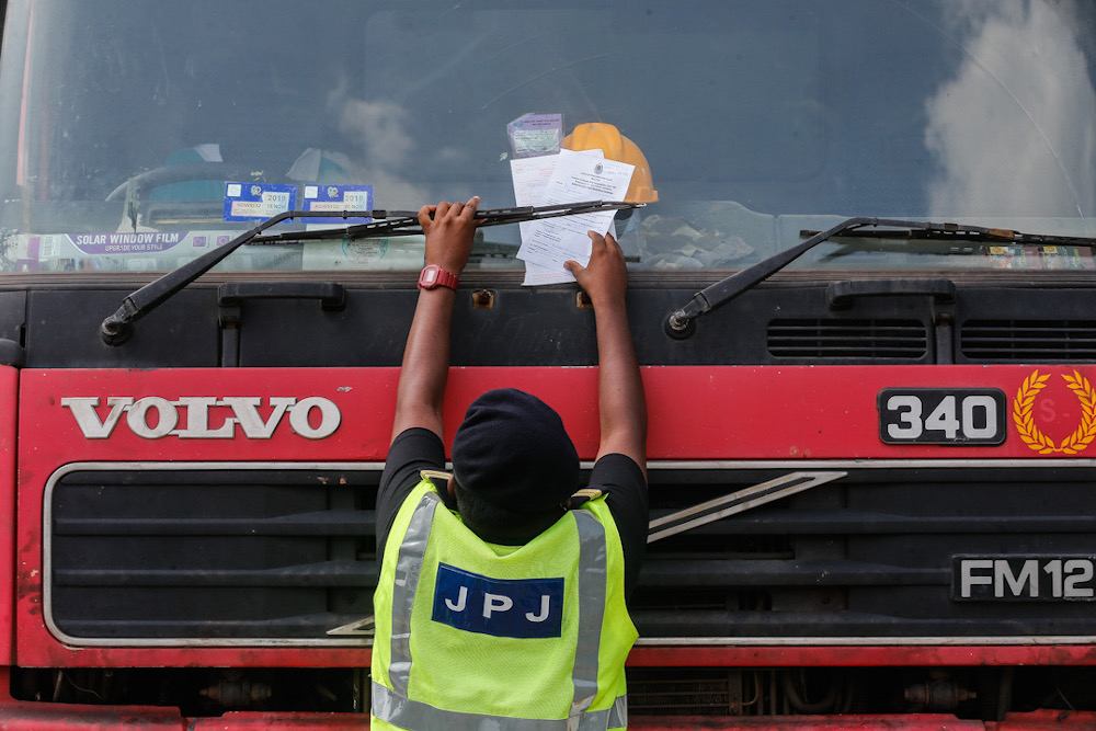 A Road Transport Department officer places a summons on a lorry believed to be breaking the rules on transporting goods at Sungai Dua, Penang, July 21, 2020. u00e2u20acu201d Picture by Sayuti Zainudin