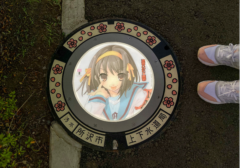 A passerby stands next to an illuminated manhole cover with designs of popular animation character from u00e2u20acu02dcThe Melancholy of Haruhi Suzumiyau00e2u20acu2122 on the street in Tokorozawa, near Tokyo, Japan August 19, 2020. u00e2u20acu201d Reuters pic