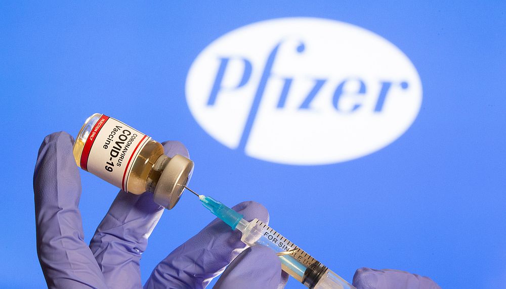 A woman holds a small bottle labelled with a 'Coronavirus COVID-19 Vaccine' sticker and a medical syringe in front of displayed Pfizer logo in this illustration October 30, 2020. u00e2u20acu201d Reuters pic