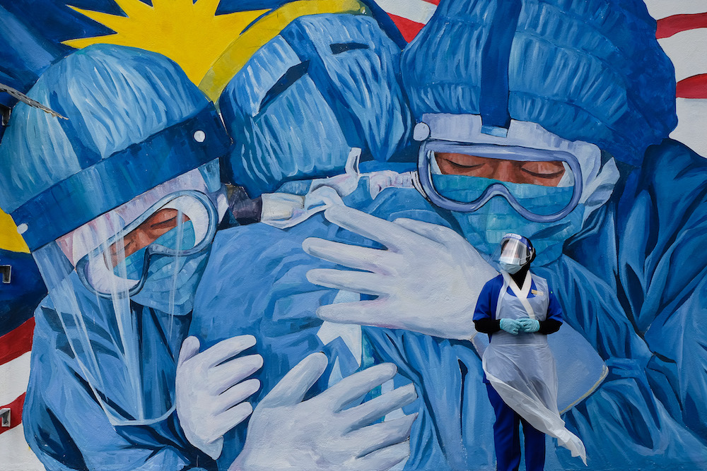 A medical worker wearing personal protective equipment rests in front of a mural featuring frontliners outside a clinic in Shah Alam December 6, 2020. u00e2u20acu201d Picture by Yusof Mat Isa