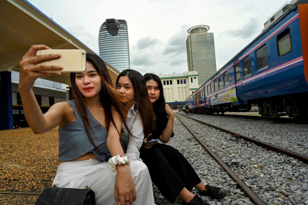 nWomen posing for a selfie next to a train at a railway station in Phnom Penh. u00e2u20acu201d ETX Studio picn