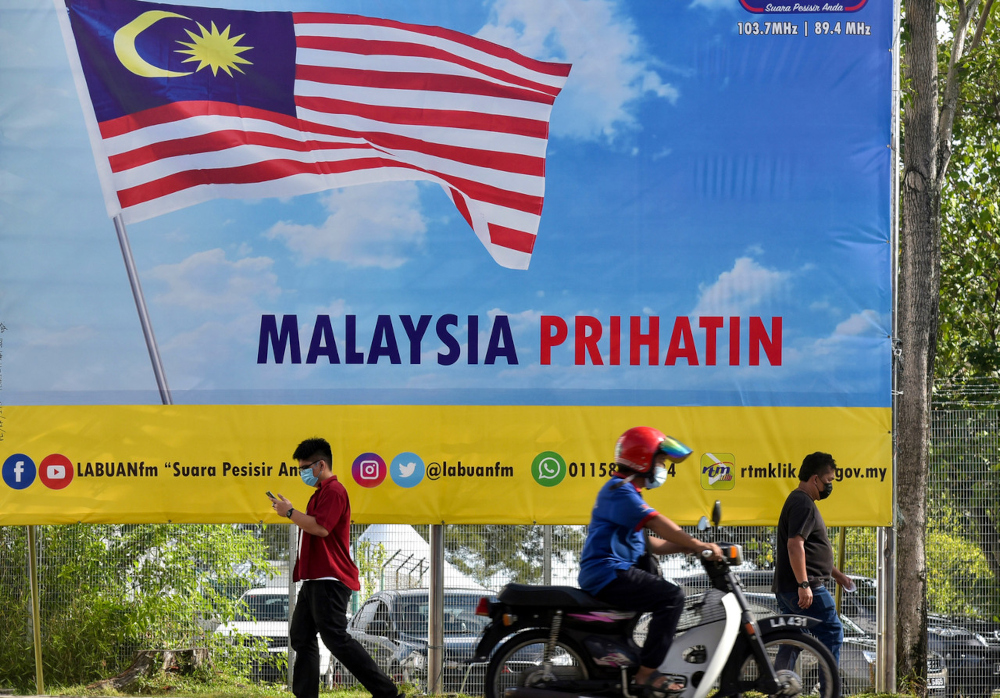 People pass by a Jalur Gemilang and Malaysia Prihatin poster in conjunction with the 64th National Day in Jalan Merdeka in Labuan town, August 19, 2021. u00e2u20acu201d Bernama pic 