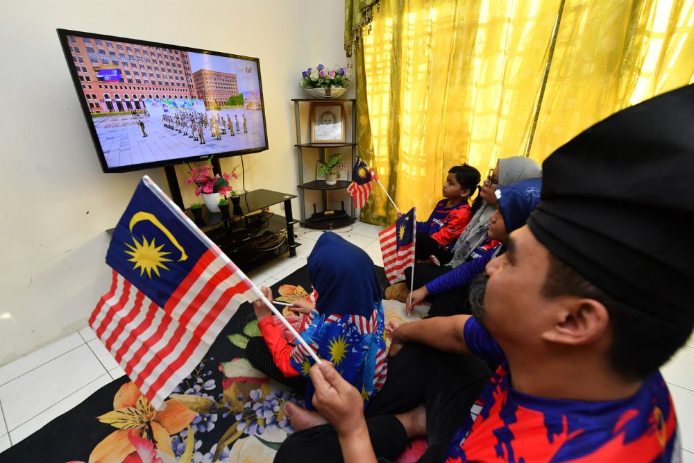 A man and his family watch a live broadcast of the National Day celebrations in Putrajaya August 31, 2021. u00e2u20acu201d Bernama pic