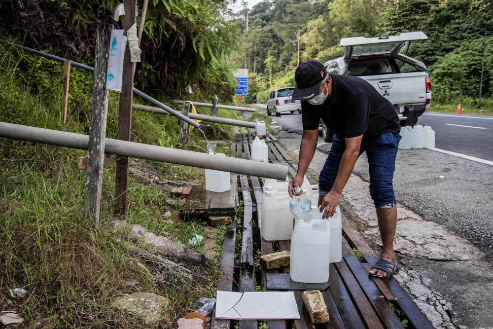 A man refills water containers from hill water during water supply disruption in Jalan Ulu Yam, October 13, 2021. u00e2u20acu201d Picture by Firdaus Latif