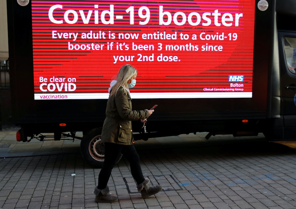 A woman wearing a face mask walks past a mobile advertising screen encouraging people to get a Covid-19 booster vaccine in Bolton, Britain, December 18, 2021. u00e2u20acu201d ETX Studio picnnnn